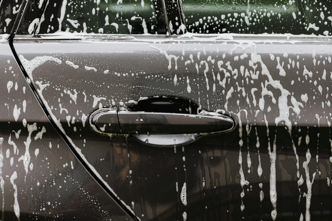 Close-up of a car door covered in soapy water during a wash, highlighting the importance of regular detailing for paint protection.