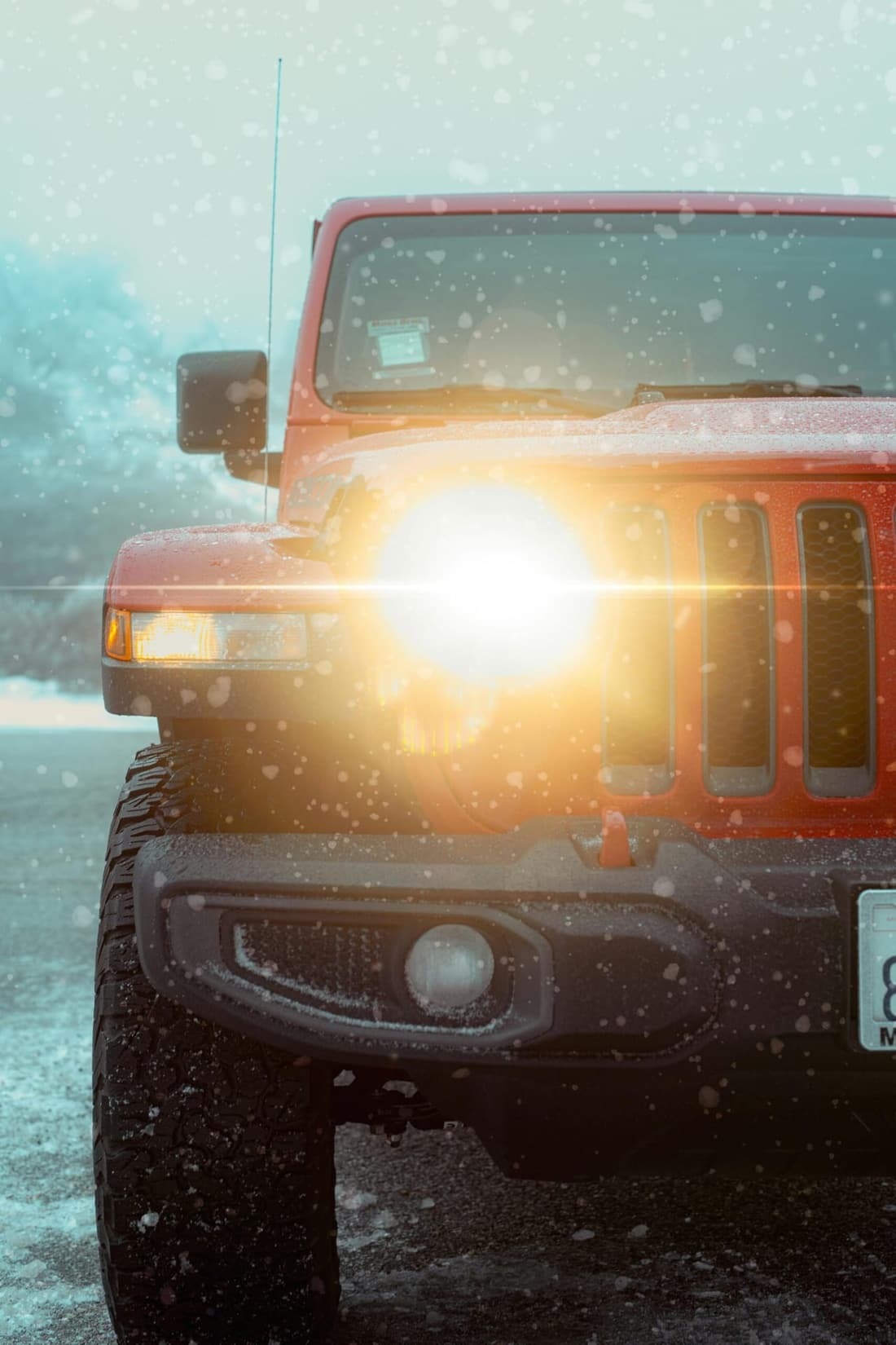 A red Jeep with headlights on, covered in snow during a winter storm.