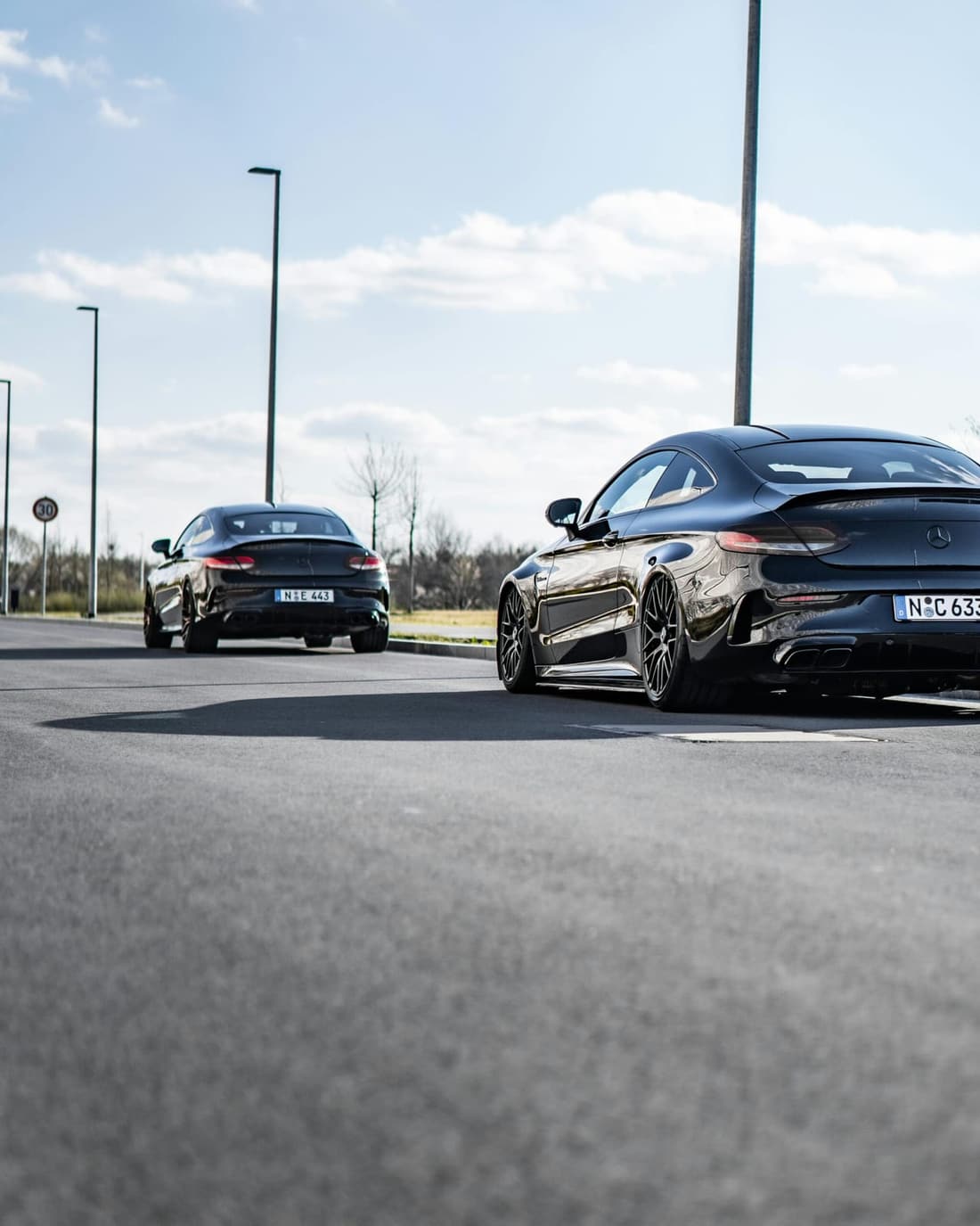 Two professionally detailed black Mercedes-Benz coupes with a flawless shine, parked on a smooth road under a bright sky.
