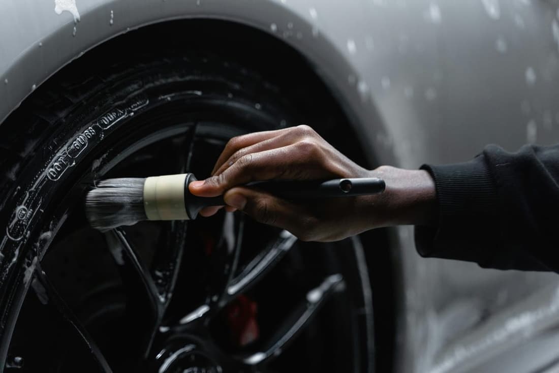 A car rim being carefully cleaned with a detailing brush by Premier Detailing, showcasing expert care and precision for a spotless finish.