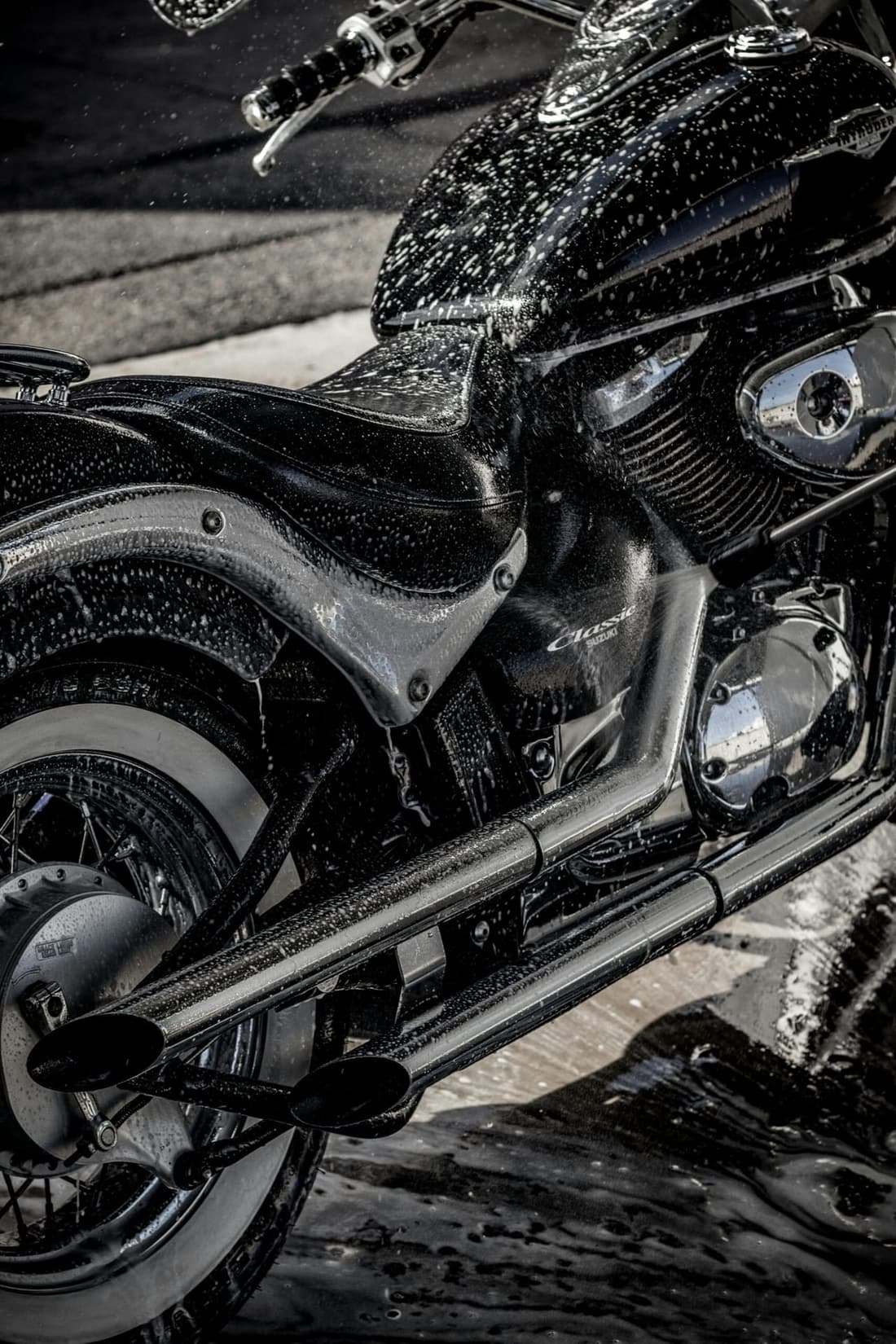 Close-up of a black motorcycle being washed with soap and water, emphasizing professional detailing.