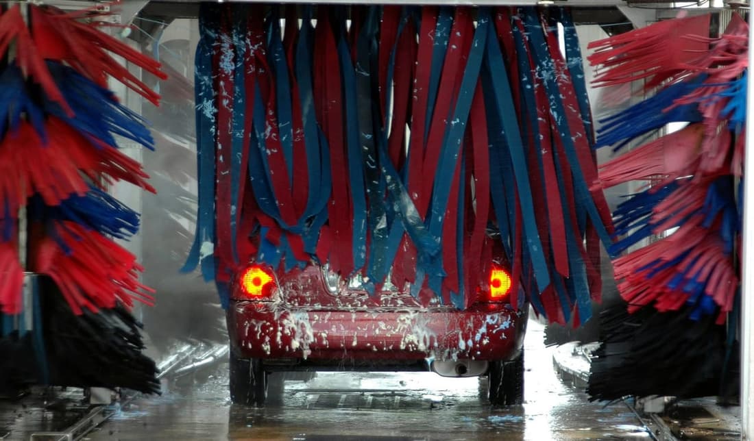 "Red car going through an automated car wash with rubber washers, highlighting the difference between automated washes and professional detailing services."