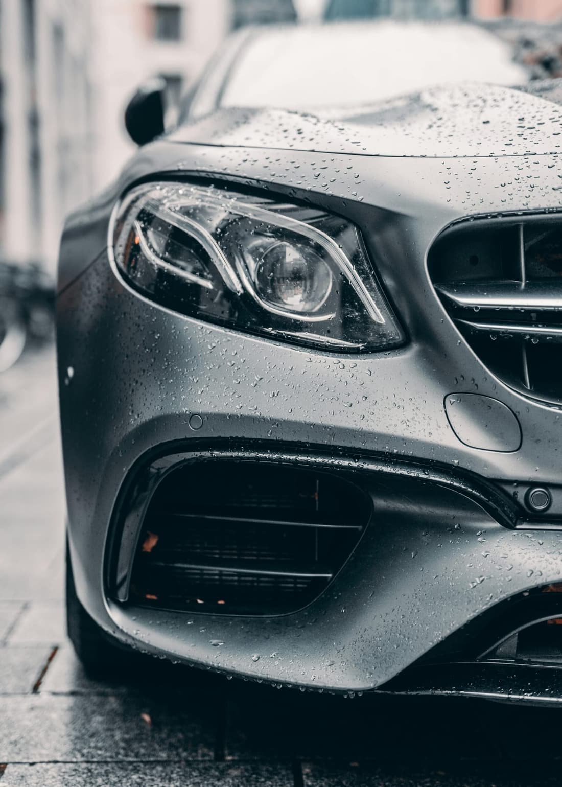 "Low-angle view of a wet grey Mercedes front left headlight, freshly washed and glistening, showcasing professional detailing results by Premier Detailing."