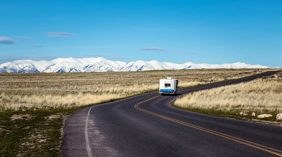 "An RV cruising confidently along a scenic road surrounded by vast fields and distant mountain ranges after a professional roof repair by Premier Detailing."