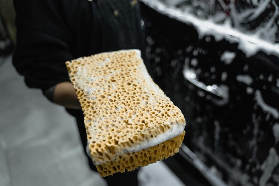 "Hand holding a wet, soapy sponge in front of a car, showcasing professional car cleaning techniques by Premier Detailing in West Plains, MO."