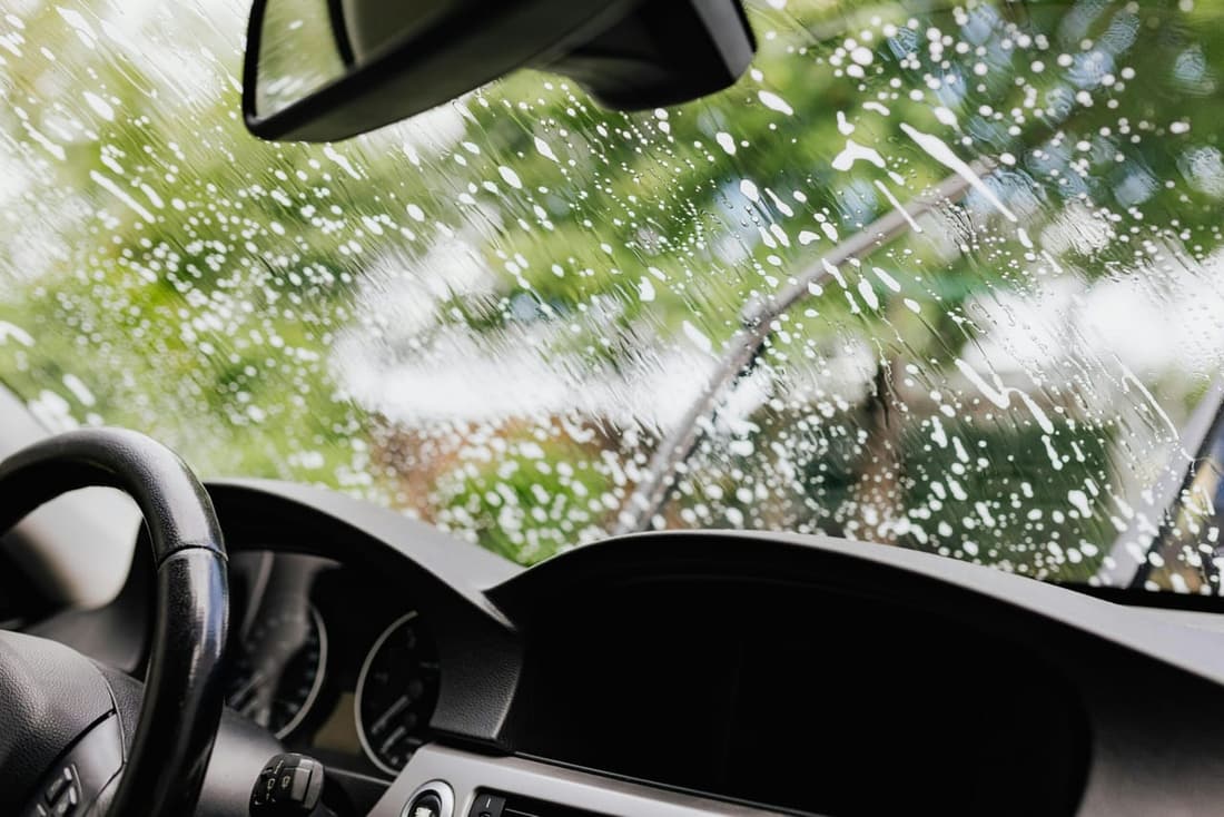 Interior view of a car during a windshield wash with soap suds and wipers in motion.