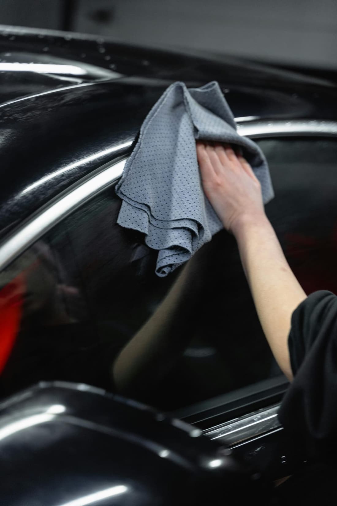 Hand wiping a black car with a microfiber towel during full detail service