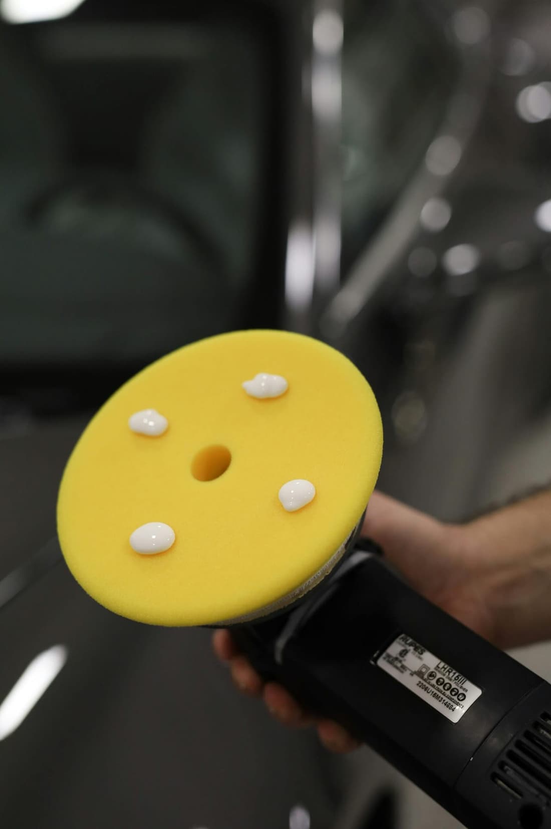 A professional-grade dual-action polisher with a yellow foam pad and polishing compound, ready for paint correction at Premier Detailing.