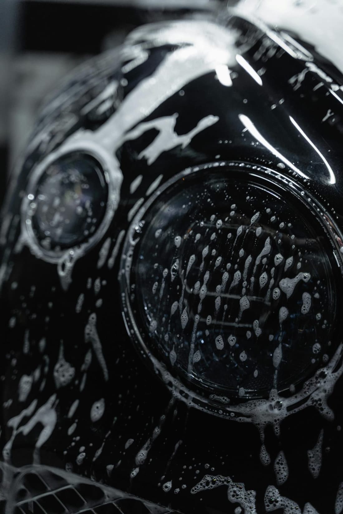 Close-up of a Bentley's headlight covered in rich car shampoo foam, showcasing Premier Detailing's expert car care services in West Plains, MO.