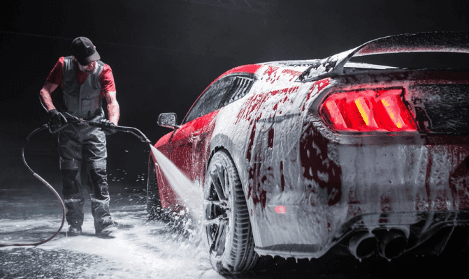 Detailer pressure washing a red sports car with foam during professional car detailing service