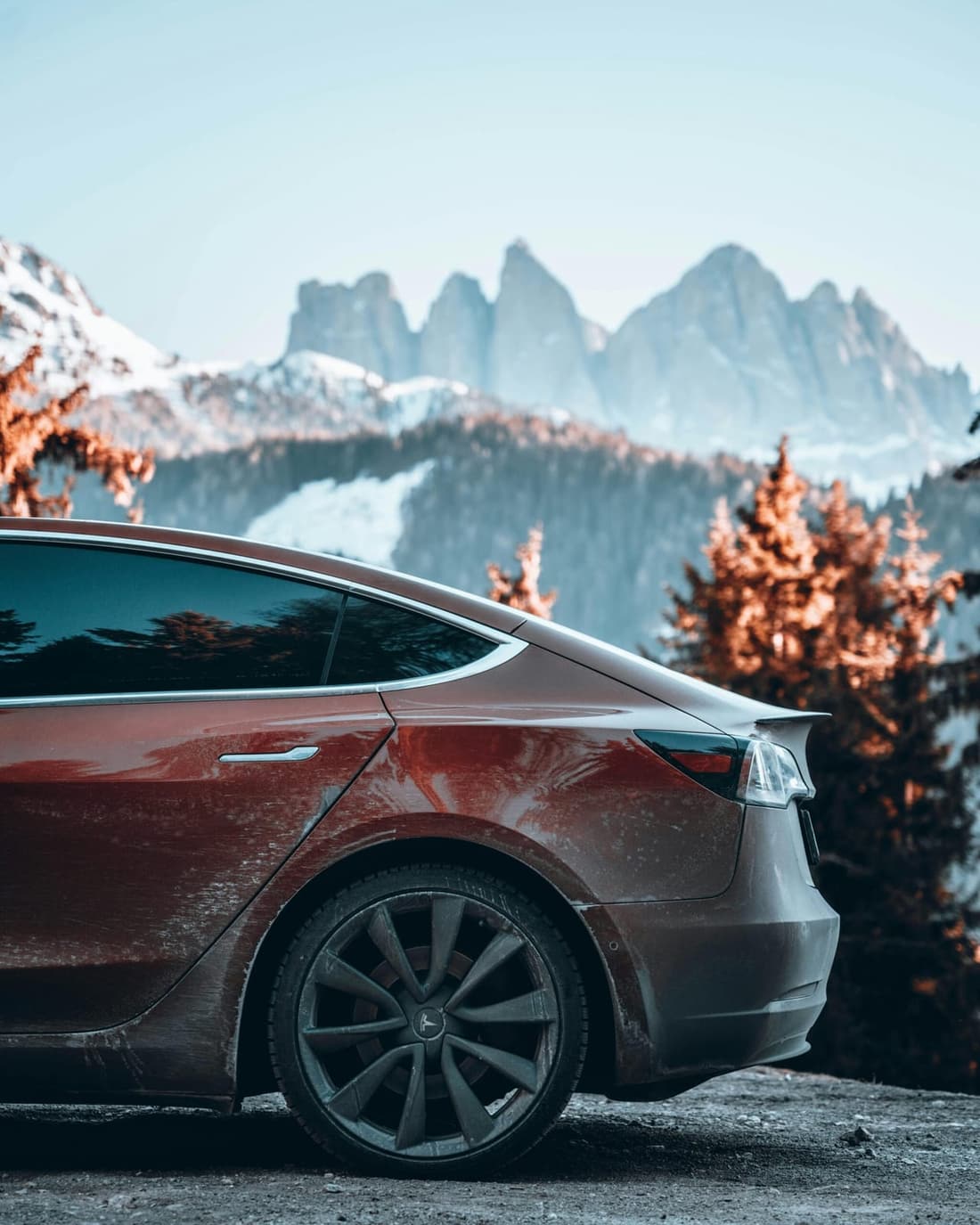 A red car covered in winter grime parked in a mountain landscape, showcasing the need for professional detailing after harsh seasonal conditions.